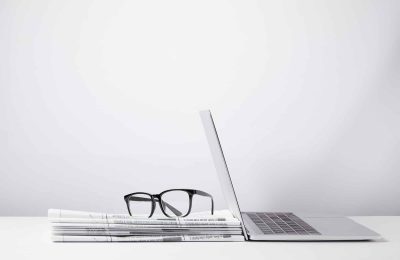 laptop and eyeglasses on heap of newspapers, on white